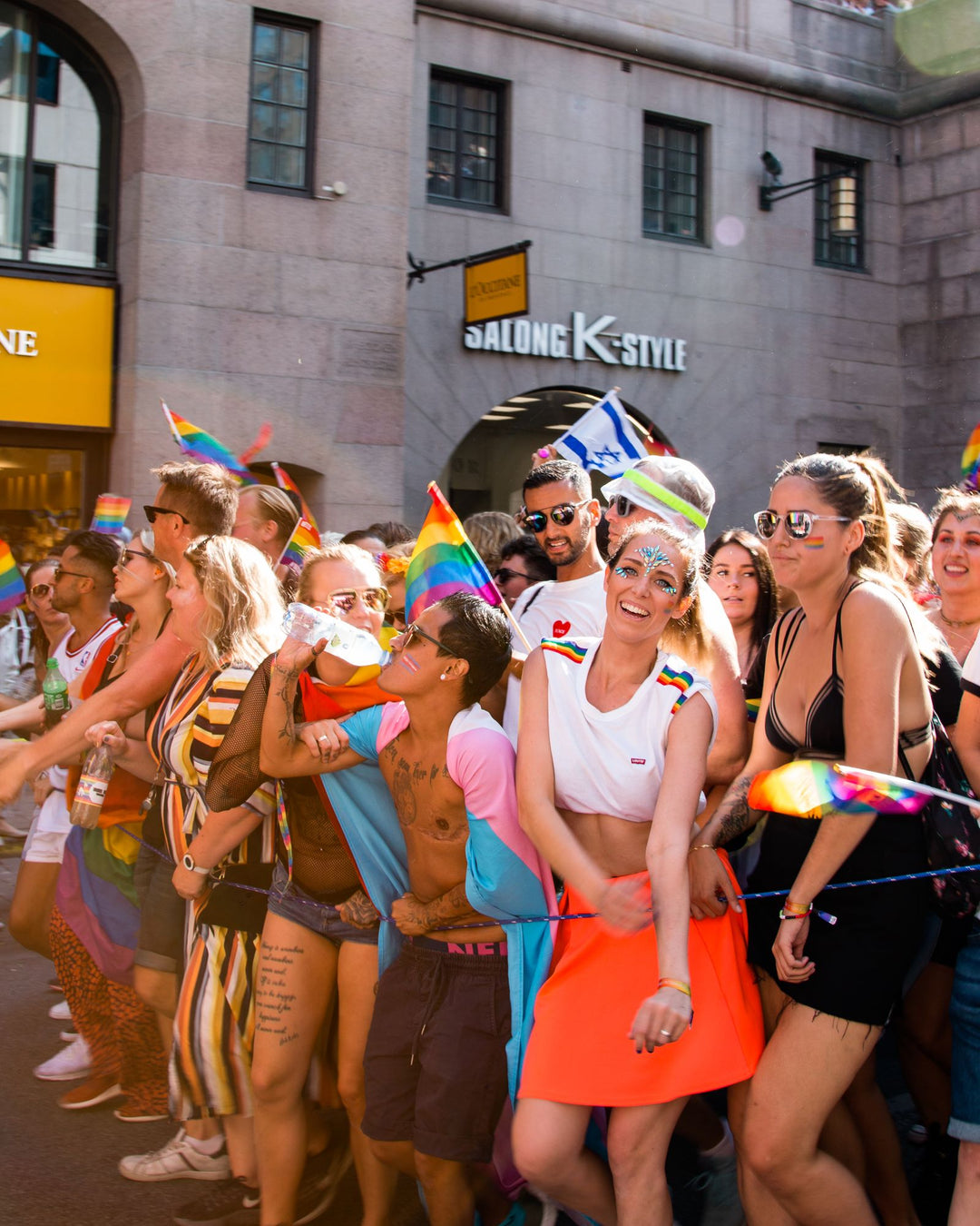 Pride crop top outfit — person styling a white crop top at a Pride celebration with rainbow flags