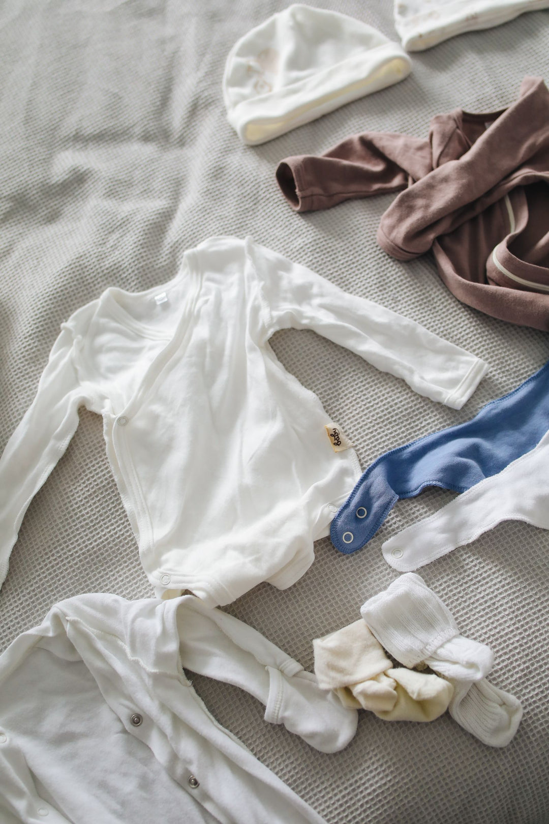 Baby onesie, hat and socks laid out on a bed — a flat lay for an LGBTQ+ baby and toddler clothes gift guide