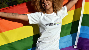 Woman with #wesaygay shirt in white with pride flag behind her
